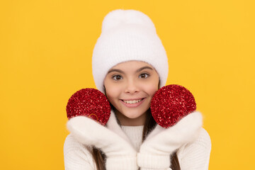 happy kid in winter hat and gloves hold decorative christmas balls on yellow background, childhood