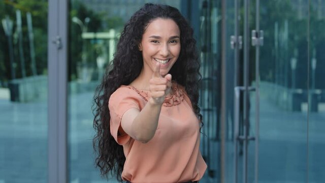 Portrait of hispanic young girl ethnic woman curly brunette female seductive lady standing outdoors points finger direction to camera makes choosing gesture say hey you choose pointing in front of her
