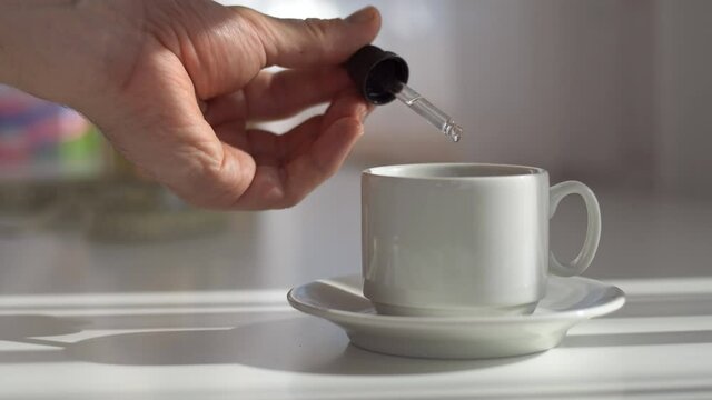 Man adding drop of cannabis cbd oil in cup of tea with pipette. Dietary supplements and vitamins. Close up.
