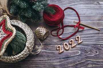 Christmas and New Year 2022 greeting card, balls of knitted yarn, crochet hook and knitted basket on a wooden table, top view