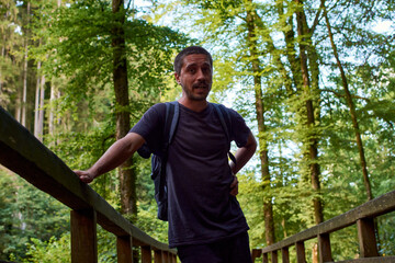 A Hispanic man with a backpack on the bridge in the forest