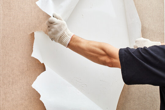 a man rips off the wallpaper to repair the wallpapering