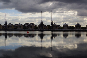 Cranes and houses reflecting in the water at London Royal Docks, London (UK)