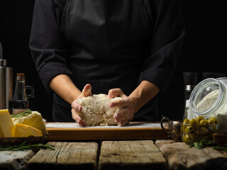 Cooking Italian cuisine. The chef kneads the dough on a wooden cutting board. Ingredients for making ravioli, pie, pizza, focaccia. Wooden background. Close-up. Step by step recipe.
