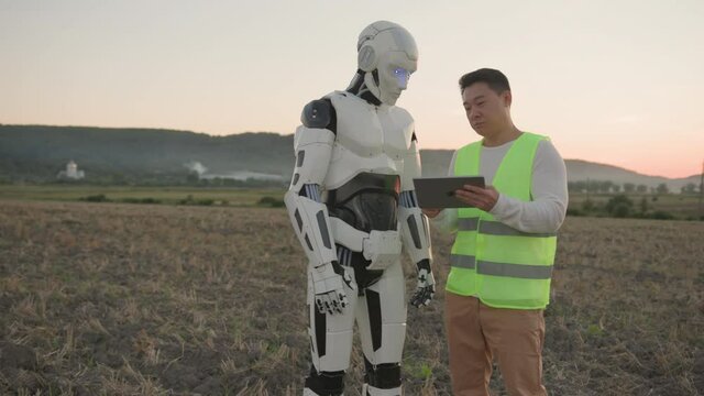 Asian engineer explaining futuristic robot to use digital tablet, showing application and discussing future work. Agricultural field. Agribusiness teamwork. AI concept.