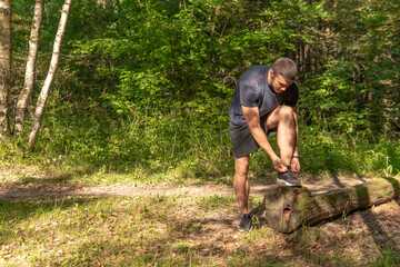 The sportsman is tying the laces of his legs in sneakers close up the athlete runs in the park outdoors, around the forest, oak trees green grass young enduring athletic athlete active forest, jogger