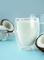 Coconut products. Cracked open coconut with meat cut in half, coconut powder in a glass jar, plant milk on a blue background. isometric projection. Copy space. Concept alternative milk, vegeterian