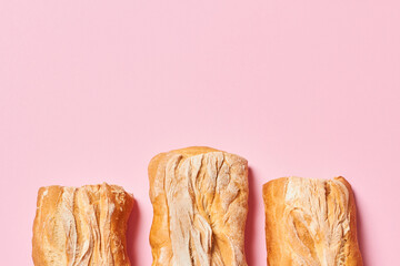 Three fresh homemade ciabatta breads on pink background with copy space. Horizontal photograph.