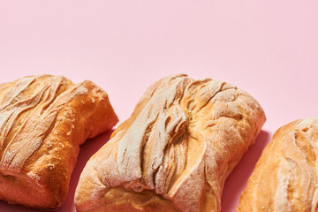 Three fresh homemade ciabatta breads on pink background with copy space. Horizontal photograph.