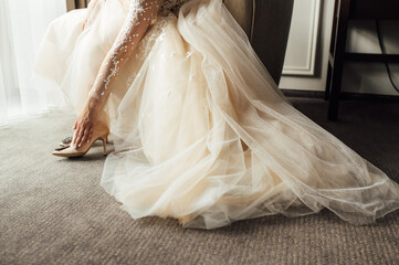 Bride with lace dress puts on her wedding shoes and straightens them with her hand