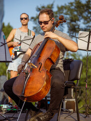 Male violoncellist playing cello in orchestra outdoors