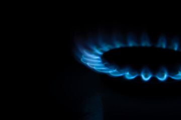 Side view of burning gas stove with blue flame in dark kitchen. Black background. Copy space for your text. Selective focus. Biogas or natural gas. Fuel industry theme.