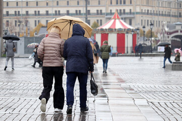 Obraz premium Rain in autumn city, couple with one umbrella walking on a street on people background