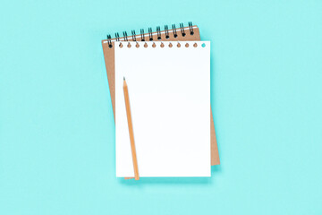 Notebook with pencil. School notebook on light blue background, spiral notepad on table. Top view of open notebook with blank pages, office notepad flat lay. White Page for your write. Copy Space