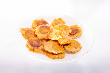 Pile of fried and smashed bananas on white background. Patacones, Tostones, chips, ripe plantain. On a white plate.