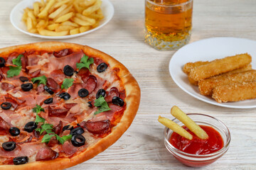 Pizza on a platter close-up on a table with ketchup, juice, sauce and fries on a white wooden table.