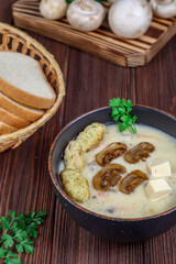 Champignon soup with parsley and croutons in a bowl on a dark wooden table against a background of mushrooms and bread.