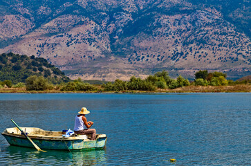 An albanian fisherman in his boat on Butrint lake salt lagoon, view from Butrint National Park, the famous UNESCO World Heritage Site in Albania, archeological site in Ksamil.