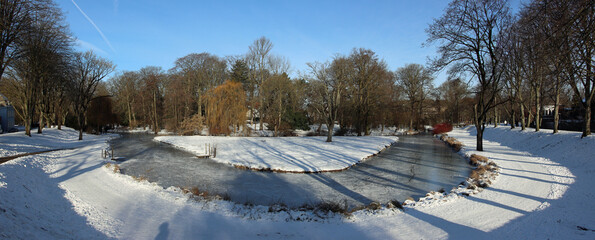 Park of the city of Moers in Germany with an icy brook and snow-covered paths with idyllic blue skies in winter  © ramonr