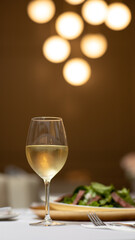 Copa de Vino blanco en primer plano con ensalada en segundo plano 