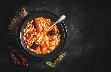 Traditional recipe of beans with chorizo and blood sausage called &ldquo;Fabada Asturiana&rdquo; on a dark table with some ingredients around. Typical Spanish food with &ldquo;compango&rdquo;. 