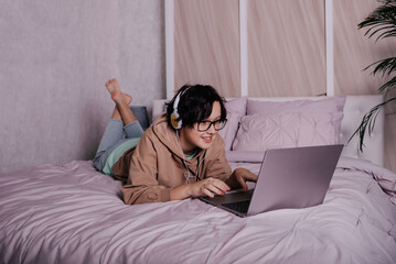 a Caucasian teenage girl is lying on the bed with headphones and a laptop