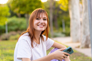 Young pretty redhead woman at outdoors holding a tablet with happy expression