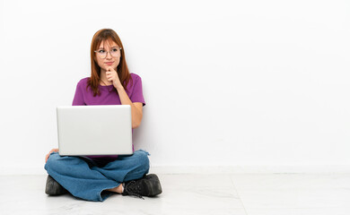Fototapeta premium redhead girl with a laptop sitting on the floor and looking up