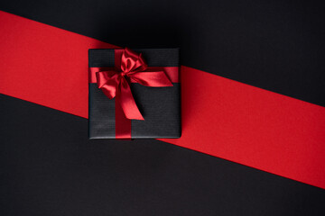 Gift box wrapped in black paper with a red ribbon and bow on a black-red background.