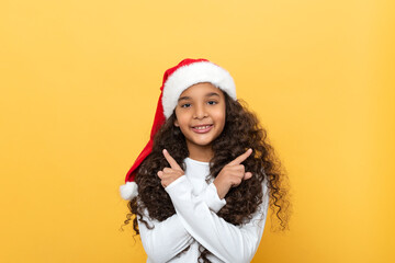 Studio shott of a dark skinned young girl with long curly hair in a Santa Claus hat on a yellow background