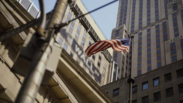 Wall Street sign with American flags in the background, shot in the heart of the business world in Manhattan. Business, finance, worldwide stock trade and economics concept.