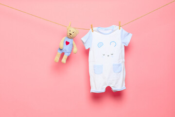 Baby clothes on a clothesline on pink background .