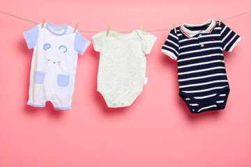 Baby clothes on a clothesline on pink background .