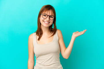 Fototapeta premium Redhead girl isolated on blue background holding copyspace imaginary on the palm to insert an ad