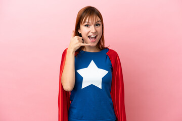 Super Hero redhead girl isolated on pink background making phone gesture. Call me back sign