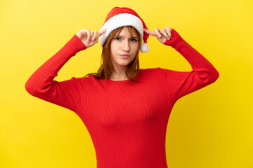 Redhead girl with christmas hat isolated on yellow background having doubts and thinking