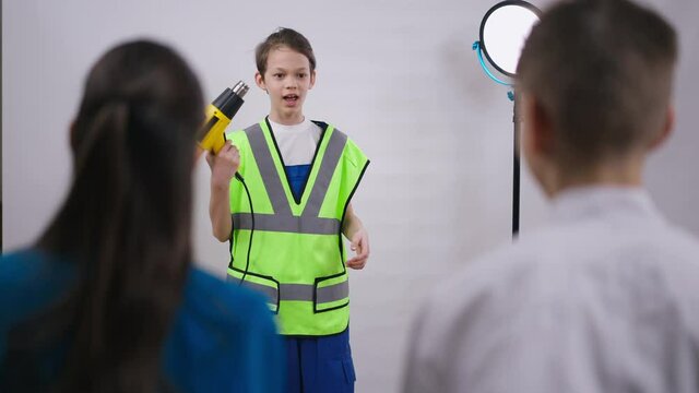 Confident little repairman explaining power drill use for friends talking at white background. Shooting over shoulder of boy and girl supporting teenager choosing profession