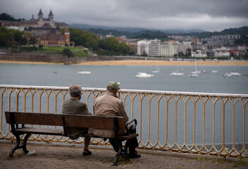 Una pareja de señores mayores de espaldas sentados en un banco mirando el mar en San Sebastian, Pais vasco. 