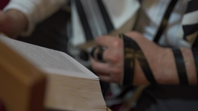 Jew reading a book. Close up of hands, tefillin, tallit