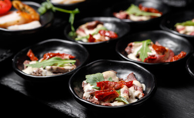 A light snack of potatoes, cucumbers, chili peppers, meat and herbs in serving cups on a dark background.