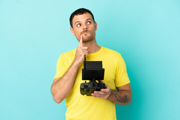 Brazilian man holding a drone remote control over isolated blue background having doubts while looking up