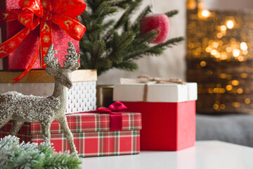 Gift boxes, spruce and deer on the table in the home interior of the living room. A cozy concept of Christmas and winter holidays in 2022. Preparation of gifts to relatives.