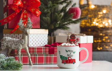 Gift boxes, a mug of hot cocoa, marshmallows and a gingerbread man on the table in the home interior of the living room. Cozy concept of Christmas and winter holidays 2022.