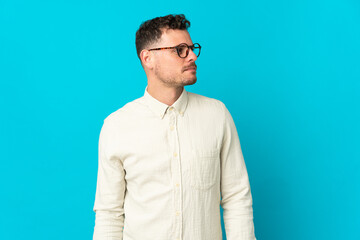 Young caucasian handsome man isolated on blue background looking to the side