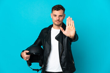 Caucasian man with a motorcycle helmet isolated on blue background making stop gesture
