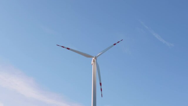 Close up of a wind turbine spinning on light blue sky on background. Ecological electricity