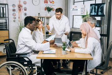 Obraz premium Focused multi ethnic doctors in medical uniform working on common research at hospital office. Male and female specialists having tensive discussion at boardroom.
