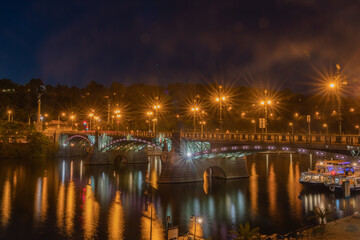 Fototapeta na wymiar Bridge across Vltava River illuminated at night with lighting reflected in water