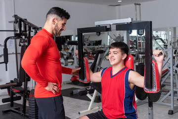 gym teacher teaching a student to do their exercises and train in a gym with machines and weights...