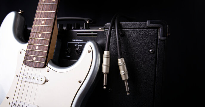Black guitar amplifier with jack cable and silver electric guitar isolated on white background